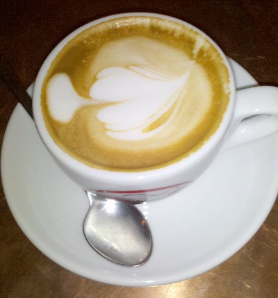 weiße Tasse mit Cappuccino auf Messingoberfläche - Schaum in Form eines Herzen